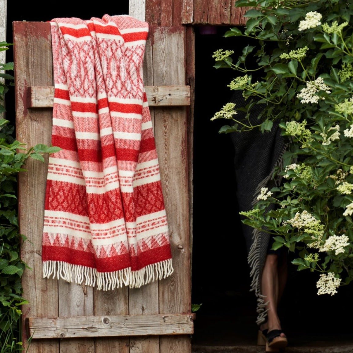 Jeté en laine Freja rouge et beige accroché sur une porte de grange