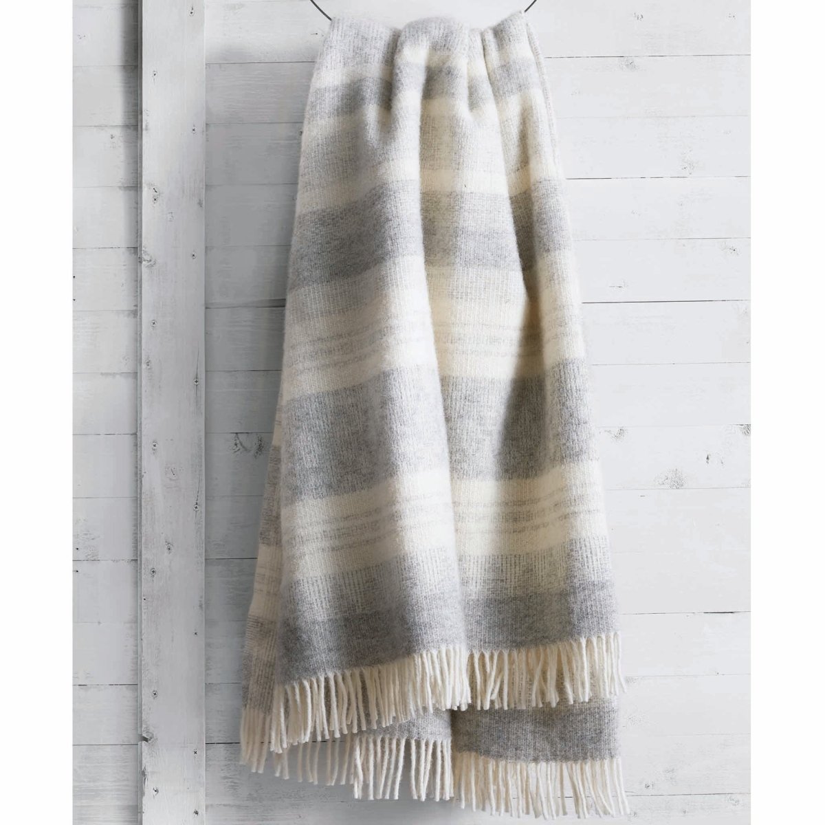 Jeté en laine Freja gris et beige sur un mur de bois peint blanc